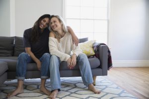 Portrait smiling barefoot lesbian couple hugging on sofa