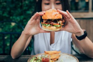 Young Woman Eating Burger At Restaurant With Outdoor Seating