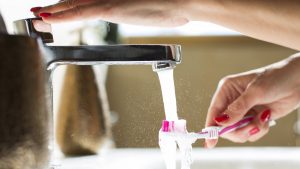 Woman rinsing her toothbrush, close-up of hands