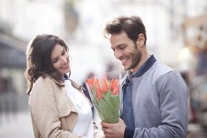 Una mujer le regala a un hombre un ramo de flores en mitad de la calle.