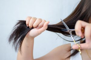 Mujer cortándose el pelo con una tijera.