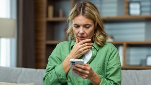 Close-up photo. Worried senior woman mother sitting on sofa at home and holding phone. Worries about children, writes and sends messages, calls, searches, waits at home