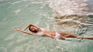 Young brunette woman in white bikini swims peacefully in the ocean