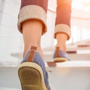 Young adult woman walking up the stairs with sun sport background.