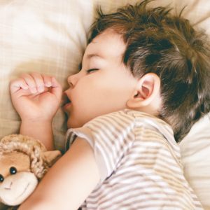 Boy sleeping on bed holding a soft toy by his side