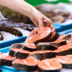 Young seller choosing a peace of salmon in the market.