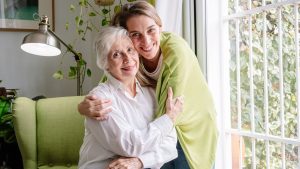 Portrait of caucasian blonde woman hugging elderly woman at home with love.