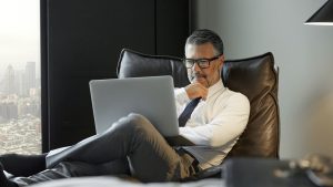Thoughtful businessman using laptop in hotel room