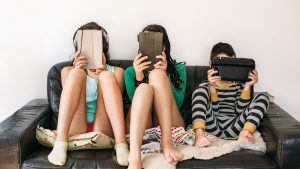 three kids with electronic devices on a sofa