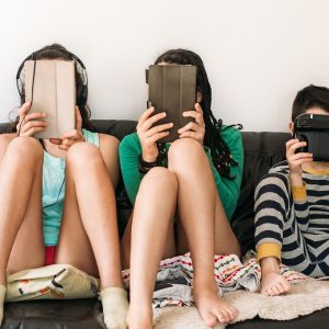 three kids with electronic devices on a sofa