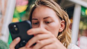 Close up of blonde girl sitting outside a restaurant table using cell phone, Side view of a cute Caucasian girl sitting outside a table texting on her smartphone