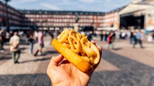 Man eating Bocadillo de Calamares (calamari sandwich) on Plaza Mayor, Madrid, Spain