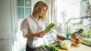 Beautiful woman unpacks a full fabric bag with fruits and vegetables on the kitchen.