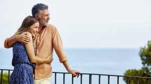 Couple embracing by railing while looking at sea